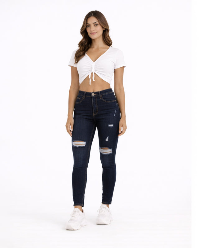 A woman stands confidently in a cropped white top and dark skinny jeans with distressed details, paired with white sn...