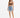 A woman stands confidently in a fitted brown crop top paired with distressed denim shorts and white sneakers.