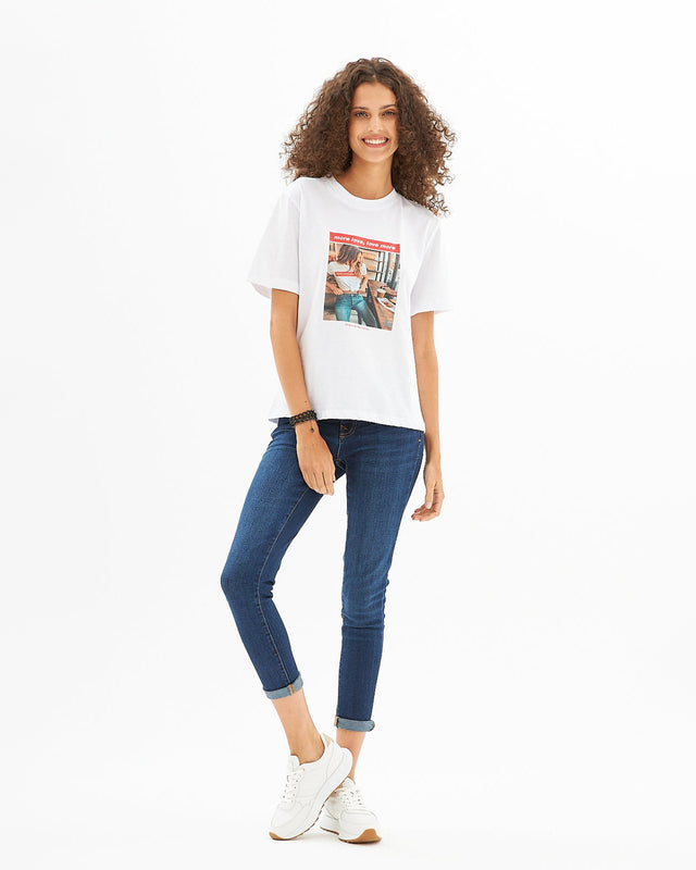 Woman in a More Love white graphic streetwear t-shirt, blue jeans, and white sneakers.