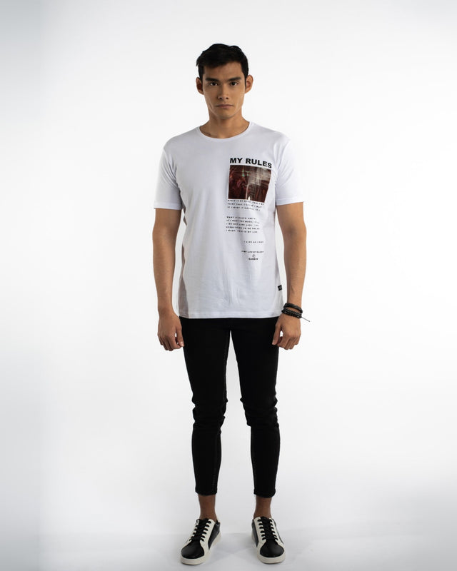 A model stands wearing a white graphic t-shirt with text and a photo, paired with black slim-fit jeans and sneakers.