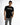 A young man poses in a black short-sleeve shirt featuring a graphic text design, paired with distressed gray jeans.