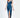 A model poses in a sleek, teal satin dress with a deep neckline and a thigh-high slit, paired with black heels.