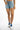 High-waisted Journi blue washed denim shorts with raw hem and distressed details, paired with white and blue sneakers.