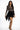 Model in Harlow black mini fringe skirt with a tan patterned long-sleeve top and heels against a white background.