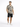 A man stands wearing a short-sleeve patterned shirt with geometric designs and black shorts, paired with white sneakers.