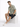 A man sits on a white pedestal wearing a patterned short-sleeve shirt and dark shorts, paired with white sneakers.