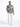 A man stands confidently in a short-sleeve, blue and beige patterned shirt paired with white jeans and sneakers.