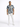 A man stands wearing a short-sleeve, blue and beige patterned shirt paired with white jeans and sneakers.