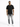 A man stands confidently in a black t-shirt, distressed gray jeans, and white sneakers against a plain background.