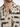 Close-up of a short-sleeve shirt featuring a beige fabric with bold black abstract patterns and a buttoned placket.
