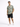 A man stands confidently in a patterned short-sleeve shirt and dark shorts, paired with white sneakers.