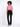 A model poses in a cropped pink top with buttons and pockets, paired with black tailored pants and heels.