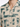 Close-up of a short-sleeve shirt featuring a beige fabric with green abstract patterns and button details.