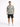 A man stands wearing a short-sleeve patterned shirt with abstract designs, paired with dark shorts and white sneakers.
