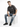 A man sits on a white cube wearing a dark gray t-shirt, blue jeans, and black sneakers, with a neutral expression.