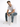A man sits on a white cube, wearing a plain white t-shirt, light blue jeans, and casual white sneakers.