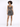 A model poses in a shimmering, fitted dress with a crisscross design and spaghetti straps, showcasing a stylish look.