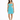 A woman stands in a fitted turquoise dress with cut-out details and thin straps, paired with black ankle-strap heels.
