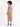 A model with curly hair poses in a fitted, knee-length dress, showcasing a sleek silhouette and strappy heels.