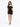 A woman in a fitted black off-the-shoulder dress with a ruched design, paired with strappy black heels.