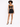 A model poses in a fitted black dress with a twist front and ruched detailing, paired with strappy heels.