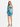 A model poses in a vibrant blue and green one-shoulder dress with a cutout and ruched detailing.