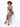 A model sits on a white pedestal wearing a fitted, patterned dress with a thigh-high slit and black heels.