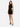 A model poses in a sleeveless black dress featuring side cutouts and crisscross detailing, paired with black heels.