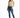 A woman stands confidently in a light green cropped top, distressed blue jeans, and white sneakers with green accents.