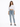 A woman stands confidently in a cropped white long-sleeve shirt and light blue jeans, paired with gray slippers.