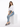 A woman sits on a white pedestal wearing a cropped white top, light blue jeans, and gray fuzzy slippers.