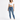 A woman stands confidently in a cropped white top and fitted blue jeans, paired with white sneakers.