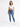 A woman stands confidently in a cropped white top and fitted blue jeans, paired with white sneakers.
