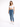 A woman stands confidently in a cropped white top and fitted blue jeans, paired with white sneakers.