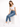 A woman sits on a white cube, wearing a cropped white top and blue skinny jeans, paired with white sneakers.