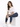 A woman with long, wavy hair sits on a white cube, wearing a casual white t-shirt and blue jeans with white sneakers.