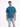 A man stands wearing a teal shirt and light blue distressed jeans, smiling against a plain background.