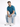 A man sits on a white cube, wearing a teal shirt and light blue ripped jeans, paired with white sneakers.