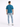 A man stands with his back to the camera, wearing a teal shirt and light blue fitted jeans.