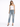 A woman poses in distressed light blue jeans with a white one-shoulder top and black high-heeled sandals.