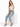 A woman sits on a white pedestal wearing light blue distressed jeans and a fitted white tank top with black heels.