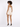 A model with curly hair poses from the back in a light-colored, sleeveless romper and black heels.