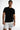 A man in a fitted black t-shirt and distressed white shorts poses confidently, showcasing a casual style.