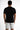 A man stands with his back to the camera, wearing a black short-sleeve shirt and white shorts with colorful paint spl...