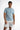 A man stands confidently in a light blue short-sleeve shirt paired with distressed white shorts.
