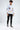 A young man stands in a white long-sleeve shirt with colorful graphics, paired with black ripped jeans and sneakers.