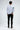 A person wearing a long-sleeve white shirt with colorful sleeve designs and black skinny jeans, viewed from behind.