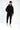A model stands in a black hoodie and matching joggers, featuring subtle logo designs, paired with white sneakers.