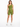 A model poses in a one-shoulder olive green top paired with matching bike shorts and white sneakers.