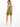 A woman in a fitted olive green one-shoulder top and matching shorts, facing away, with white sneakers.
